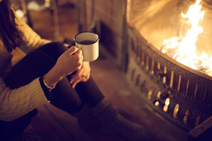 a person sitting in front of a fireplace holding a mug of tea