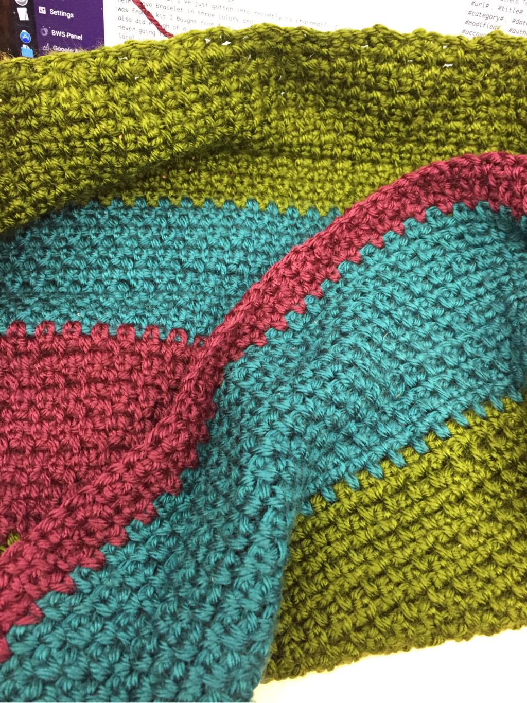 Part of a blanket, crocheted, in purple, blue-green, and green jewel tones