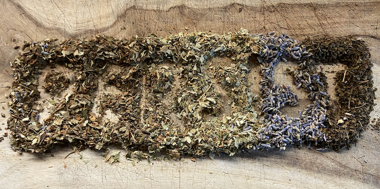 Four kinds of herbs laid out on a piece of wood, with the word "persist" traced in them.